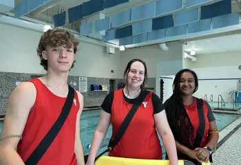 three smiling Y Winnipeg lifeguards next to a pool