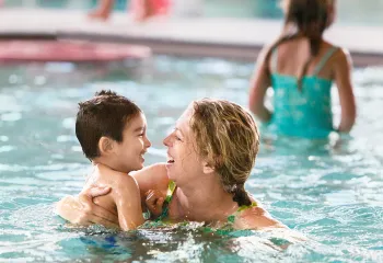 smiling woman in pool with small child in her arms