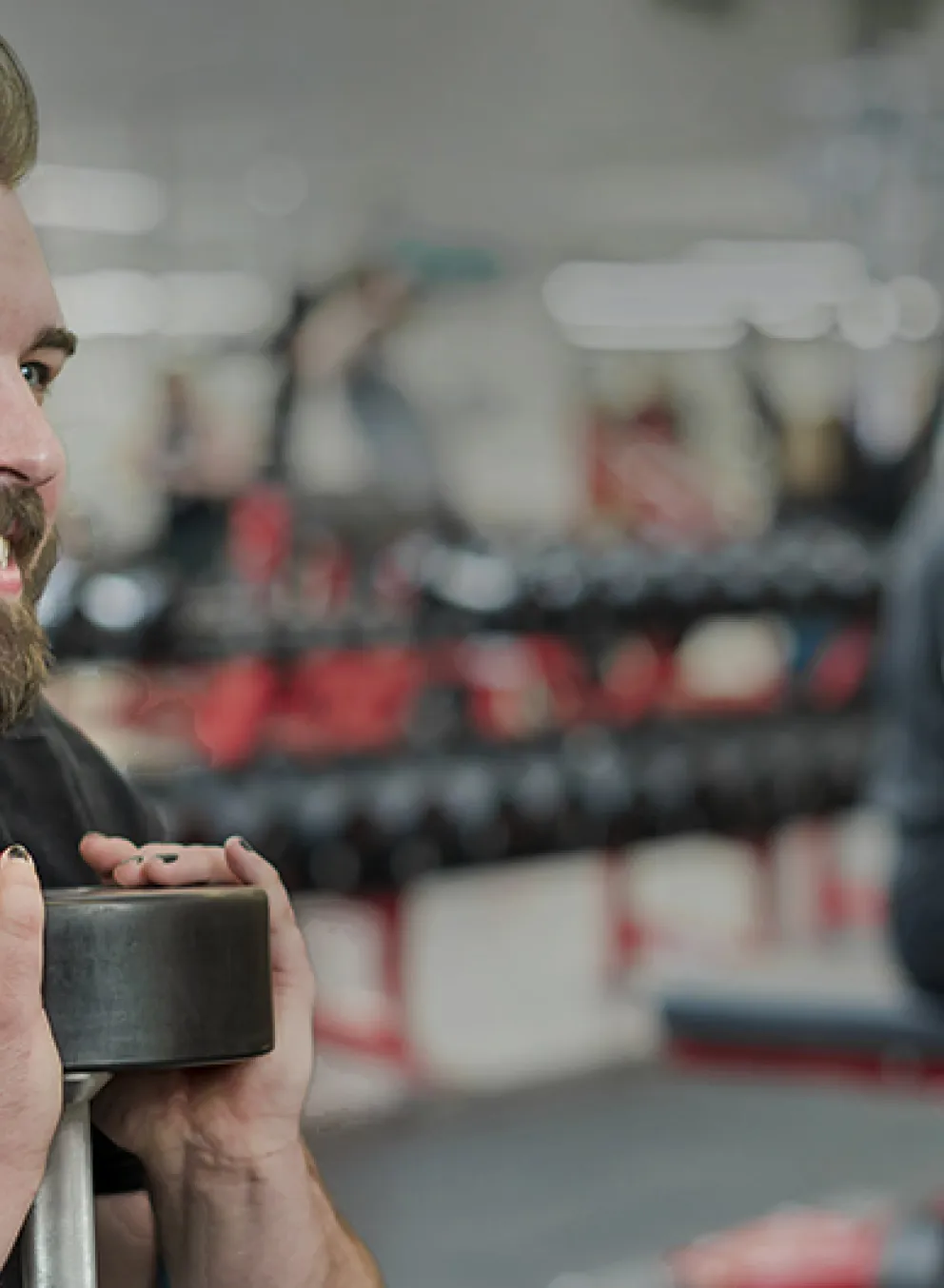 Smiling brearded man holding a dumbbell doing a squat