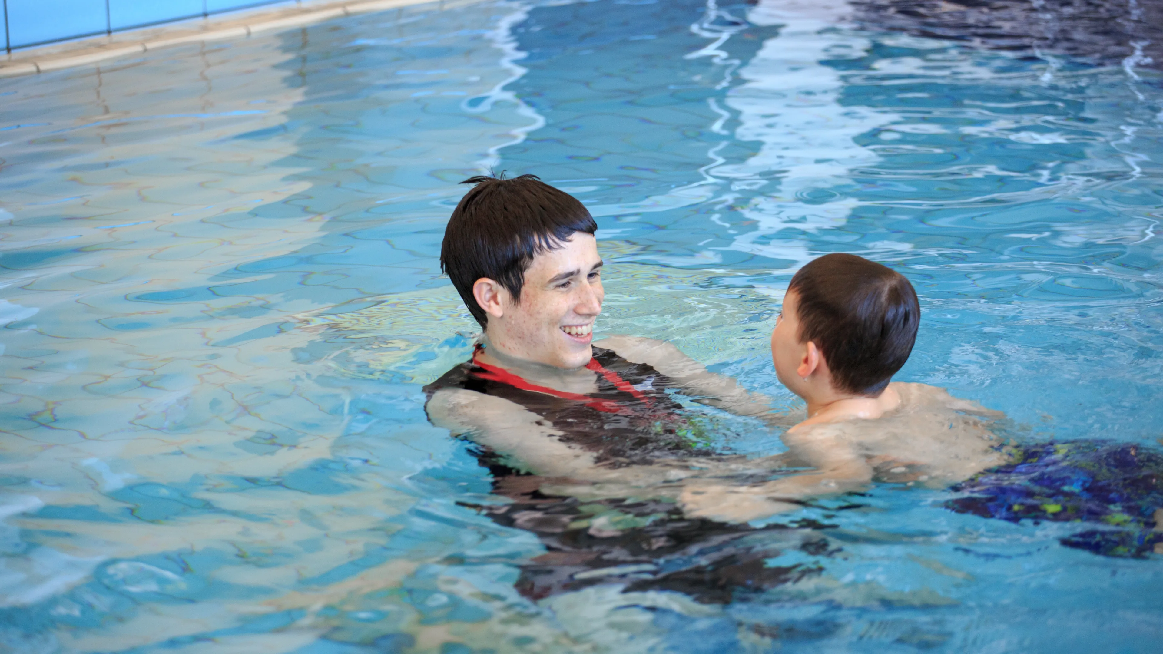 smiling male swim instructor teaching young swimmer in pool