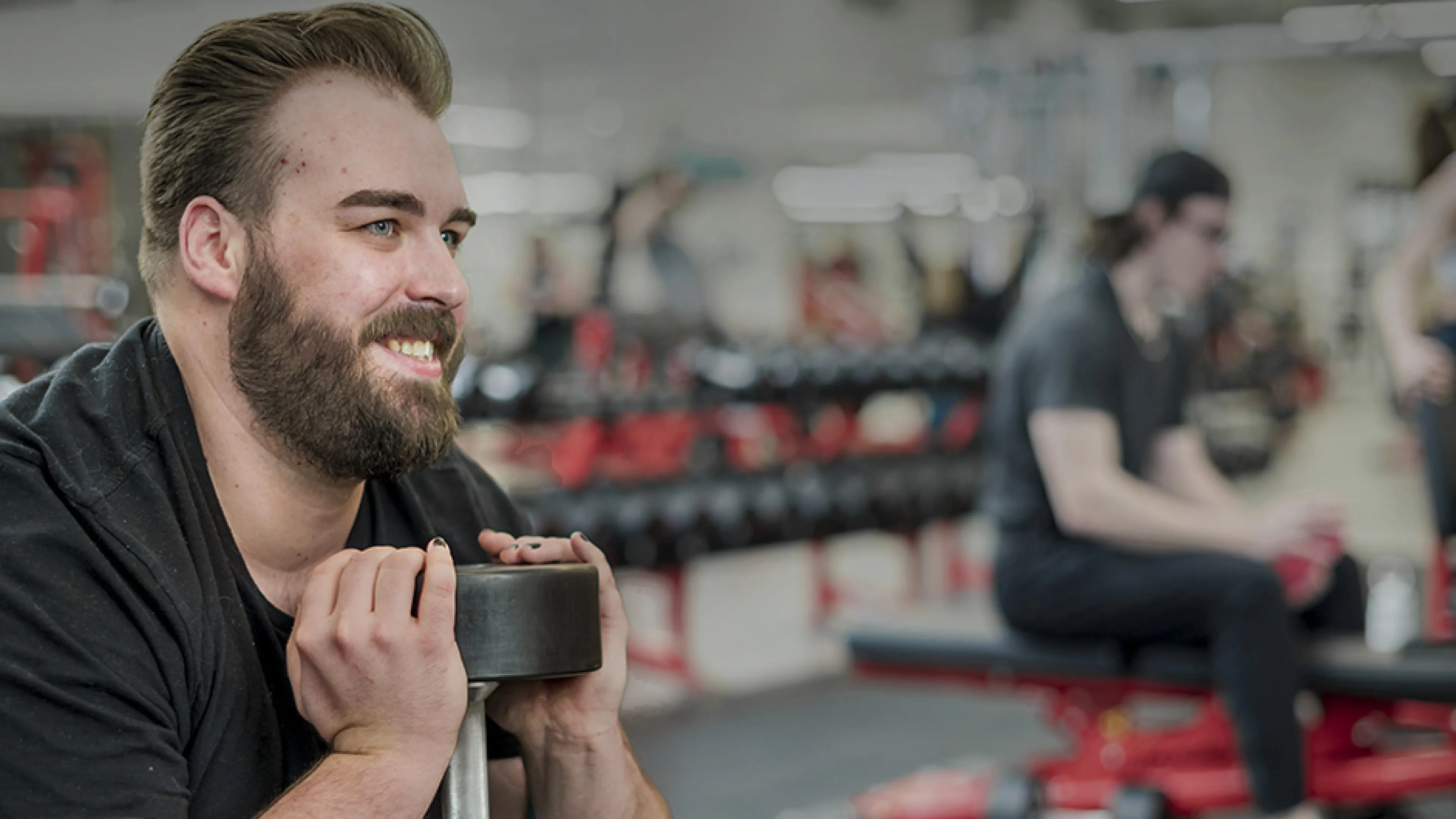 Smiling brearded man holding a dumbbell doing a squat