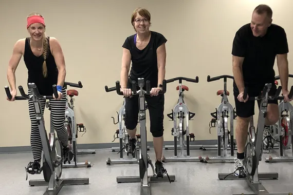 Photo of Alisa (left) indoor cycling with her mother and father