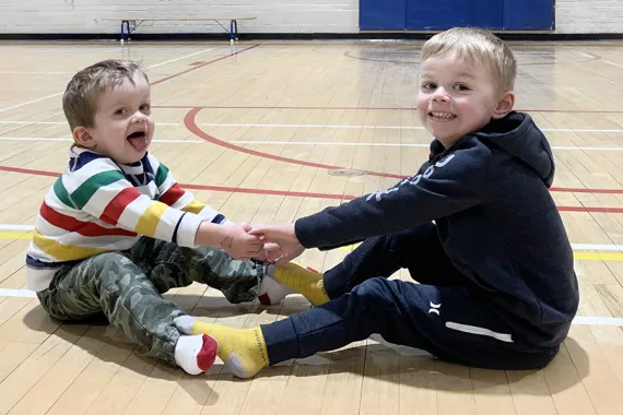 Photo of Alisa's two kids holding hands and playing on the gym floor at the Y