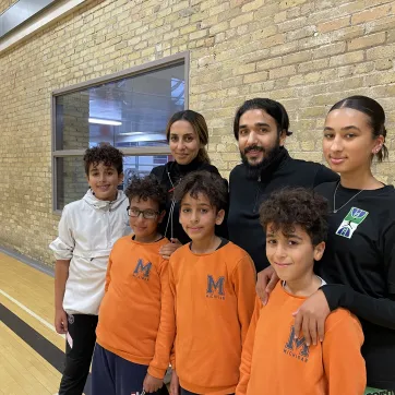 Image of the Fekiri family at the Downtown Y. Triplet boys stand in front wearing orange with older sister, father, mother and older brother in the back row. 