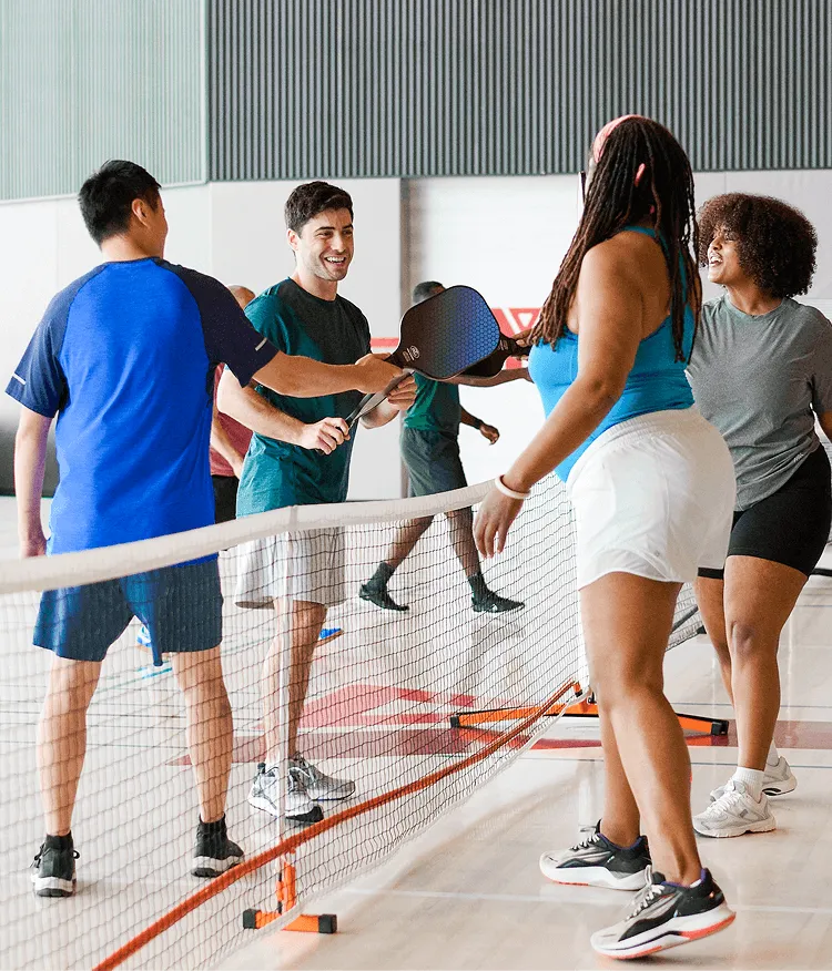 People touching pickleball paddles over a net