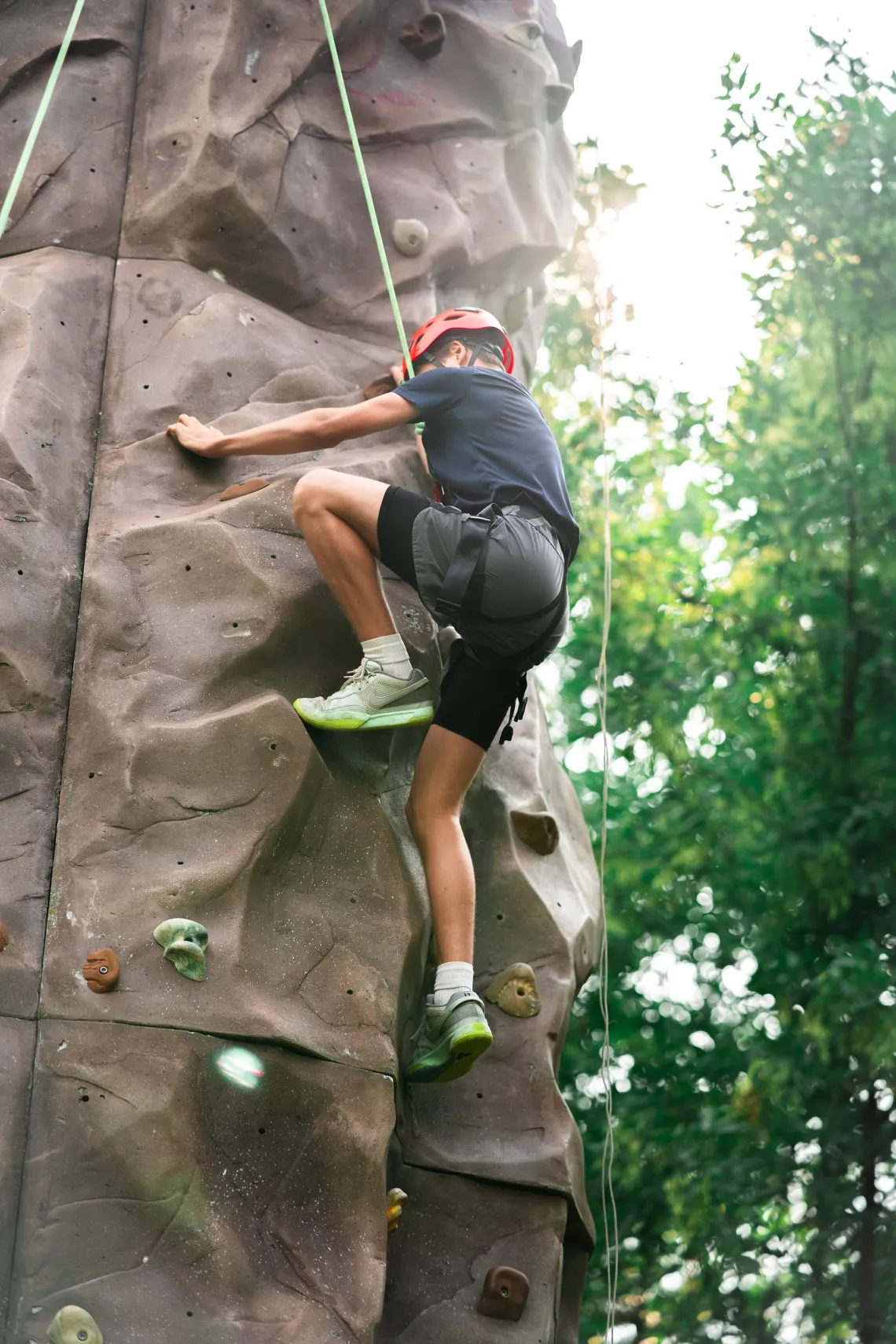 young male climbing up the rock tower while secured