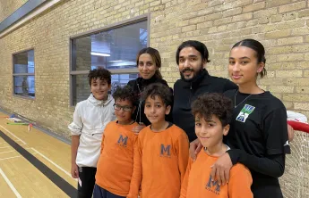 Image of the Fekiri family at the Downtown Y. Triplet boys stand in front wearing orange with older sister, father, mother and older brother in the back row. 
