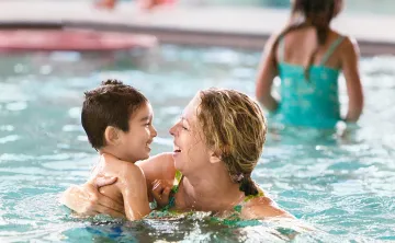 smiling woman in pool with small child in her arms